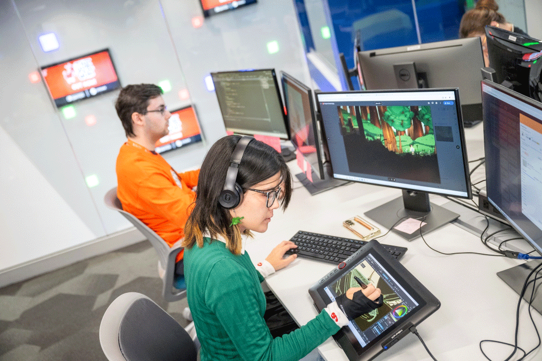Two students sit in a modern and brightly lit computer lab, working on a video game.