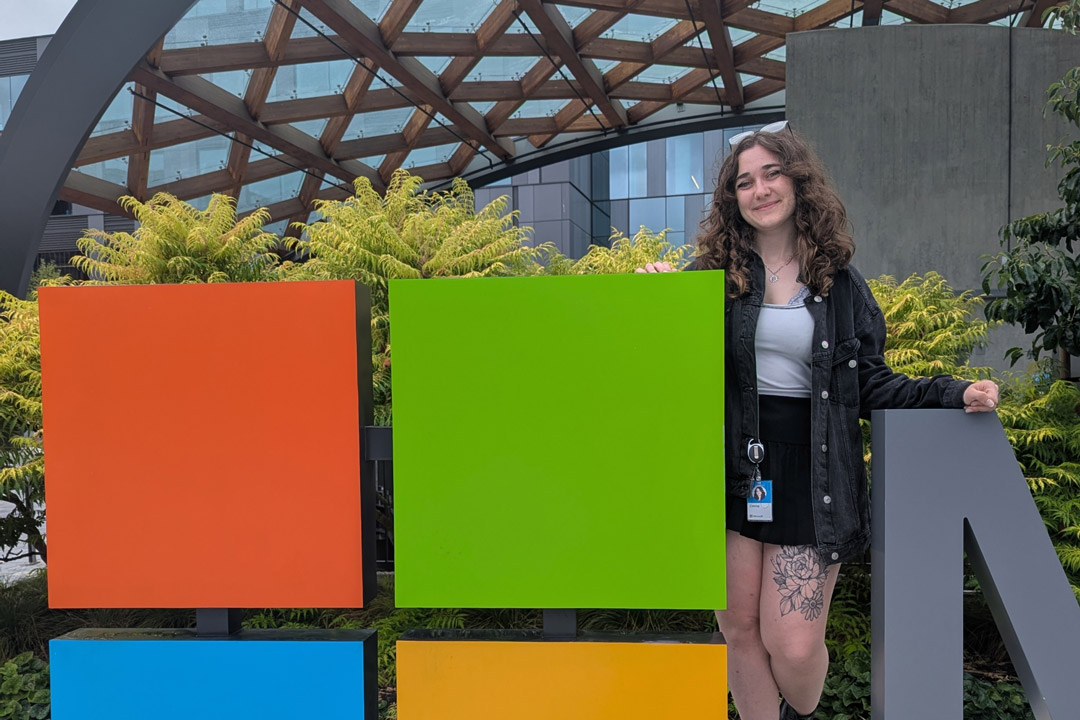 A college age woman stands next to a multi colored cube on the Microsoft campus.