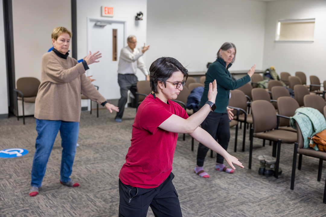 three people practive Tai Chi in a classroom environment.