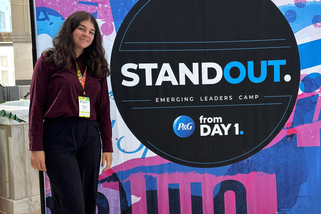a college age woman stands next to a poster for Stand Out Emerging Leaders camp