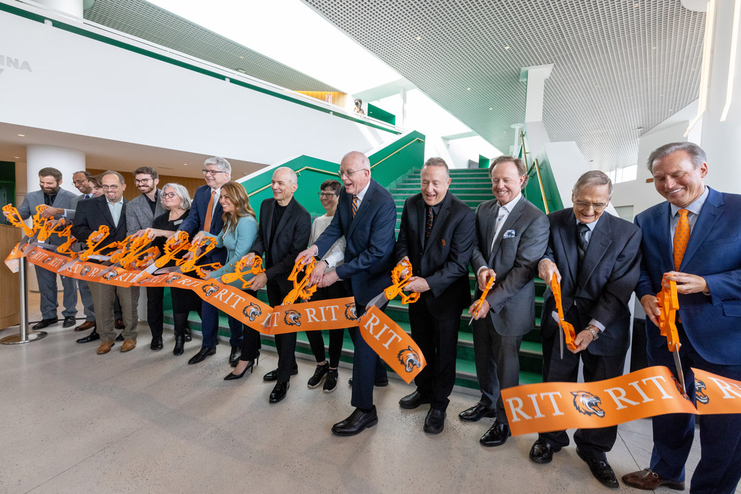 Group of officials cut orange R I T ribbon during building opening ceremony indoors