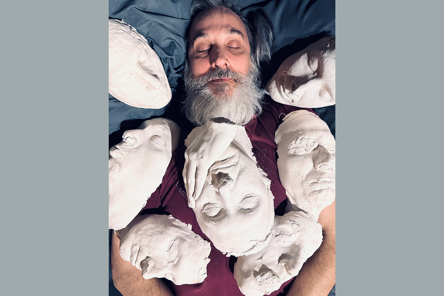 A man is surrounded by casts of his own face.