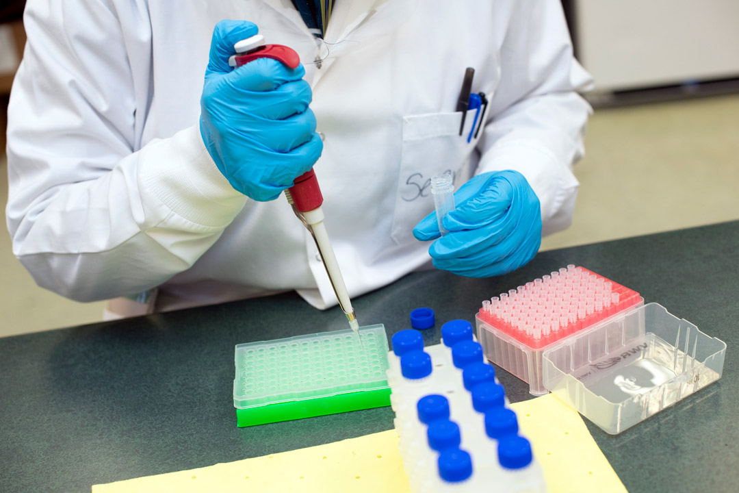 a person in a lab coat uses a pipette in a lab