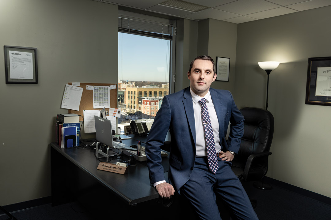 a man sits against a desk in a blue suit 