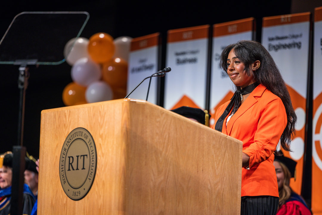 a student orange blazer as she welcomes the audience at the Gordon Field House and Activities Center for New Student Convocation