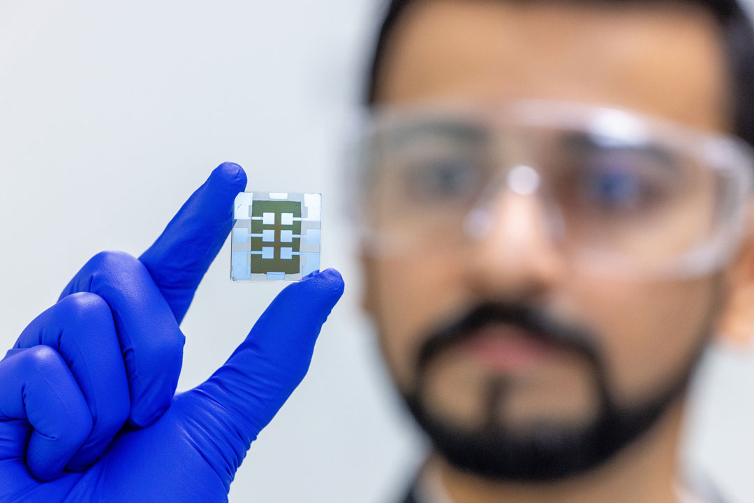 A man holds a solar cell in a blue gloved hand.
