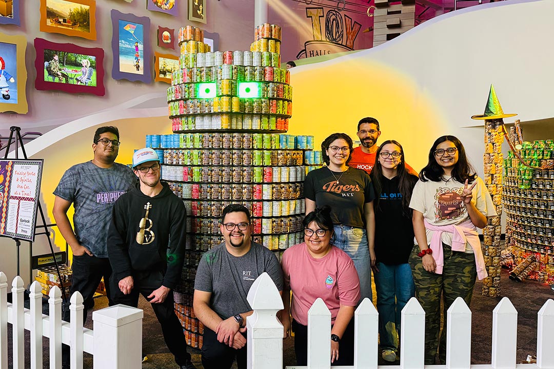 A group of students stand around an owl sculpture made out of canned food.