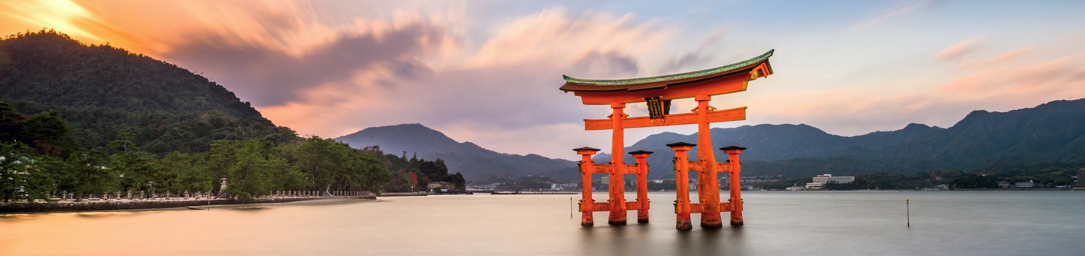 A Japanese 'torii' gateway sits in the water with mountains in the background.