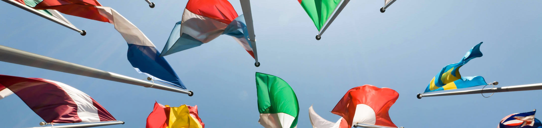 View from below of a variety of flags and blue sky.