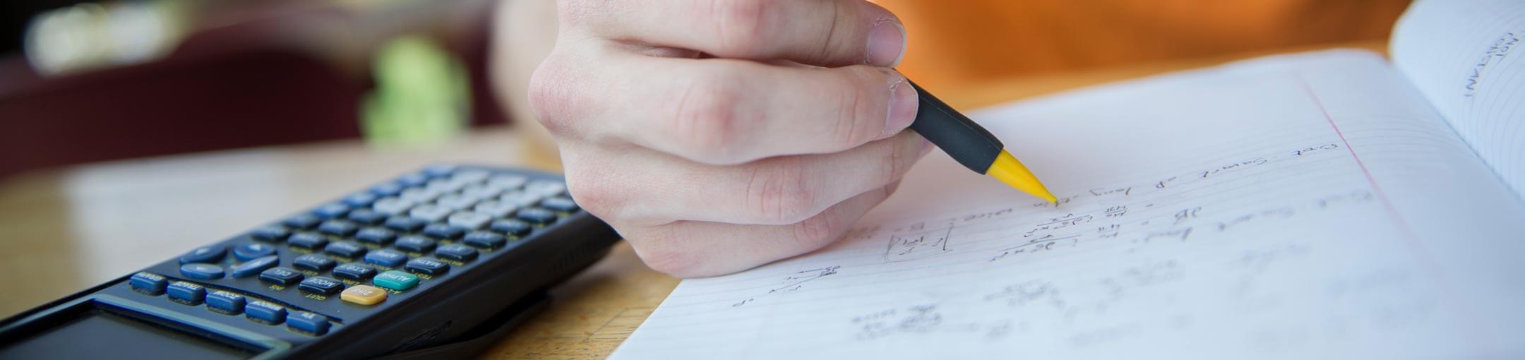 Close up of hand writing in a notebook with a mechanical pencil and a graphing calculator.