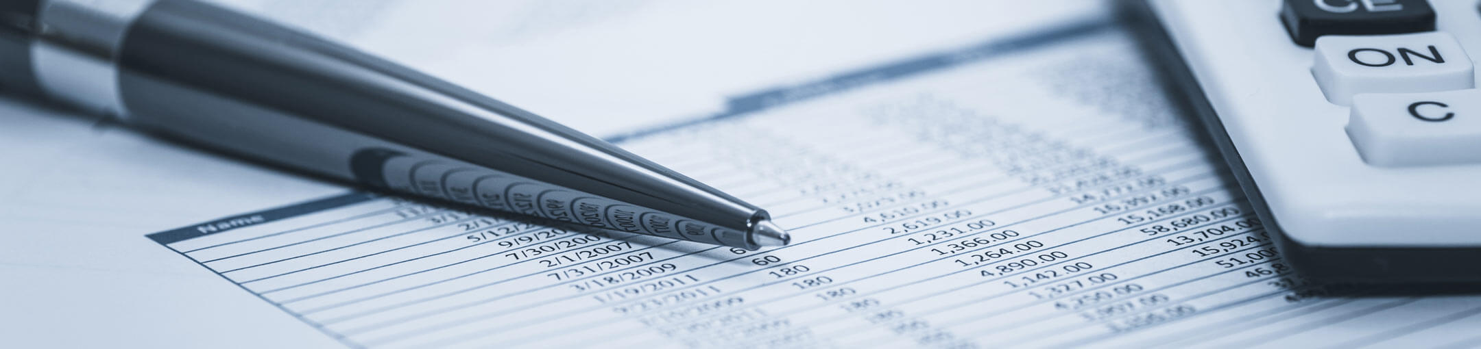 Black and white close up of pen and calculator on top of number chart.