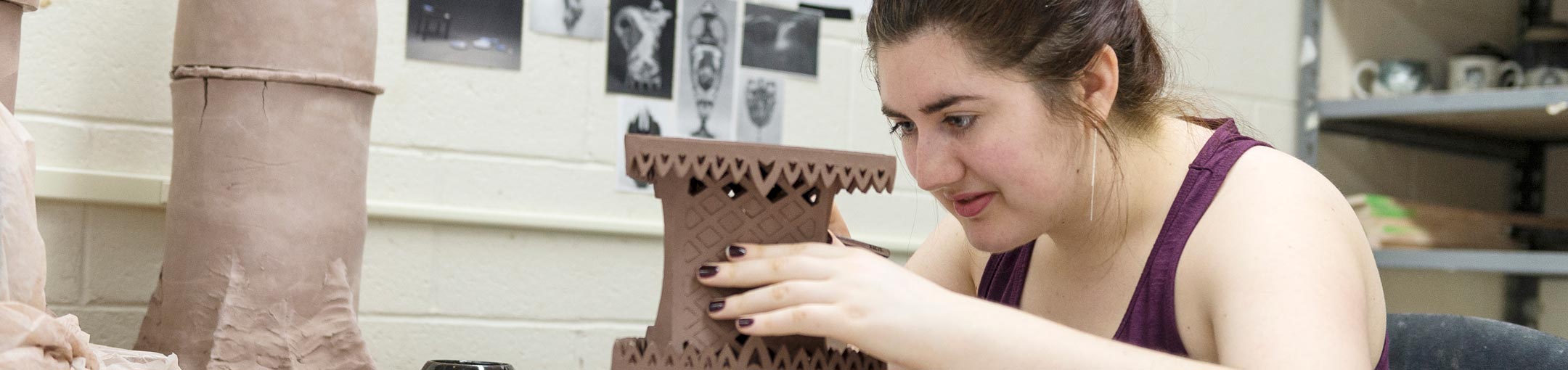 Student creating intricate lattice in ceramic sculpture.