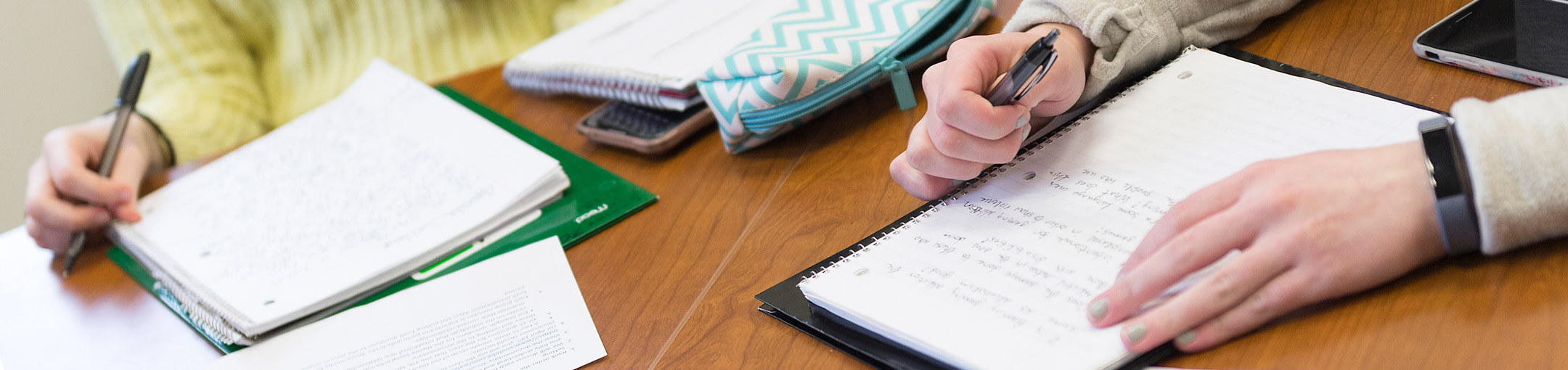 Close up of hands with pens and notebooks.