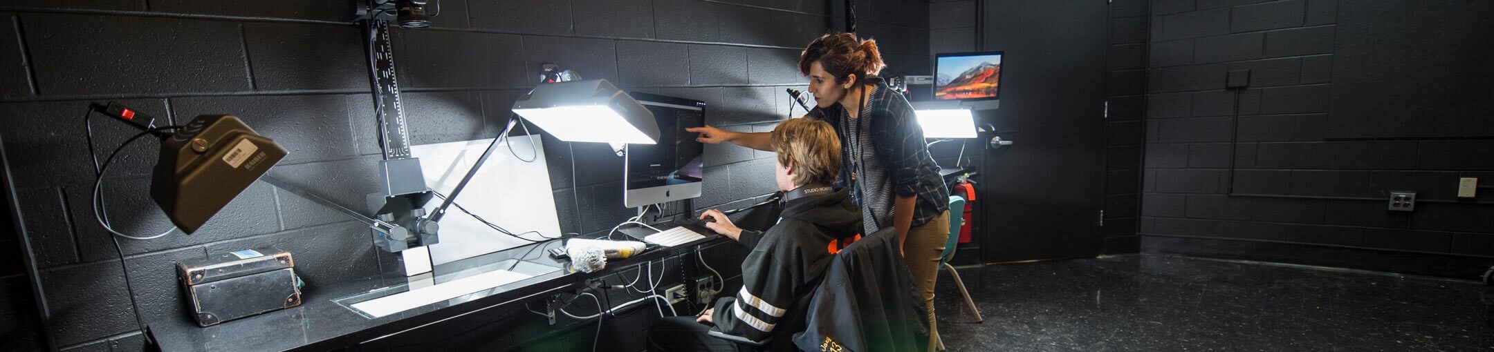 Two people in a lab with spotlights looking at a computer.