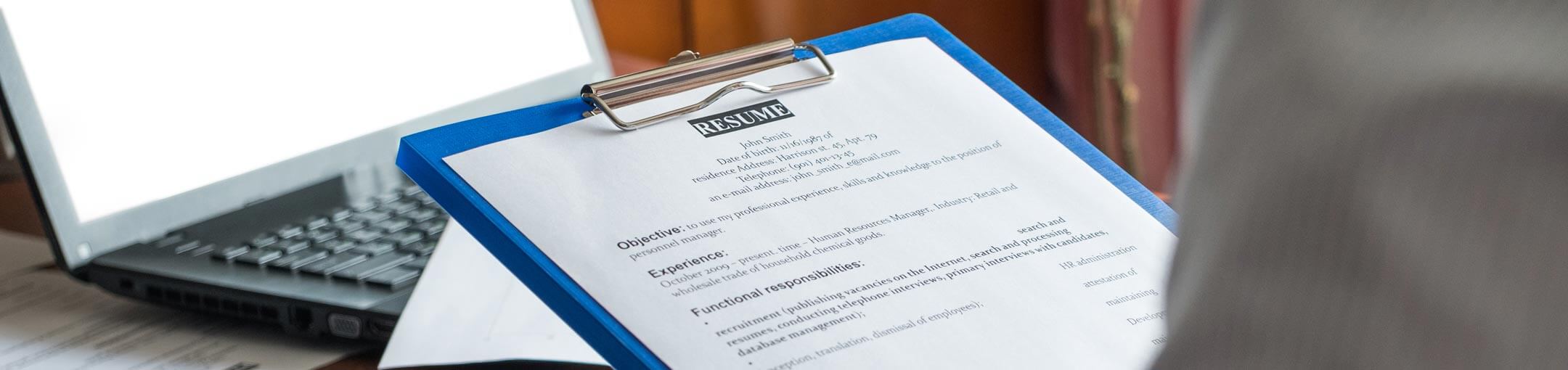 Person looking over resume on clipboard in front of laptop.