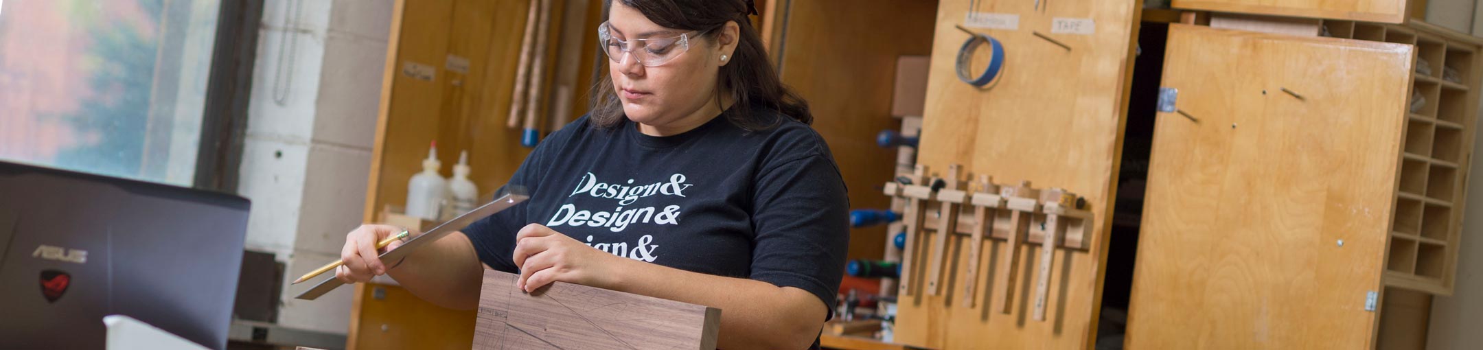 Student with ruler and pencil in hand makes measurements on a piece of wood