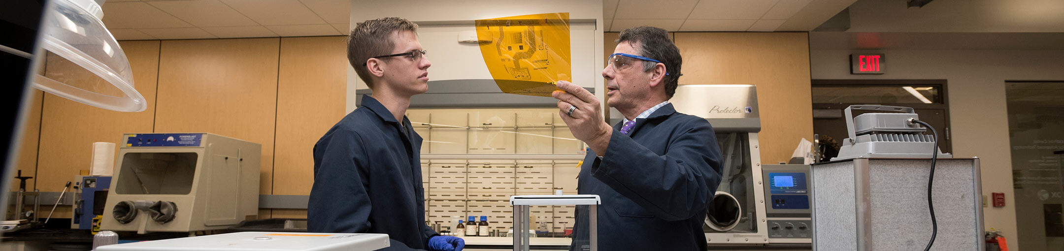 Student and professor talk over a schematic printed on amber-colored celophane.