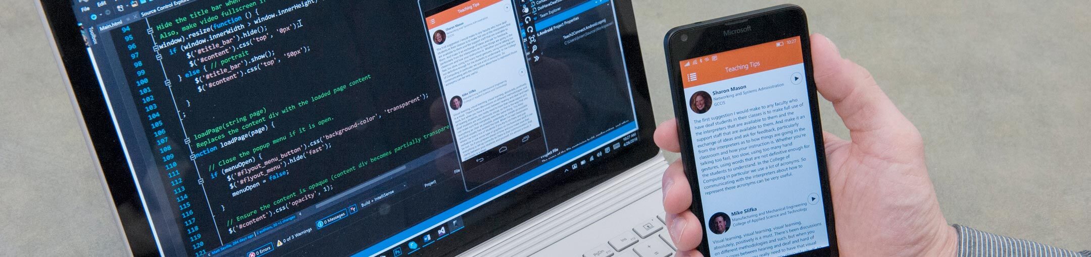 A close up of a person holding a smart phone in front of their laptop.