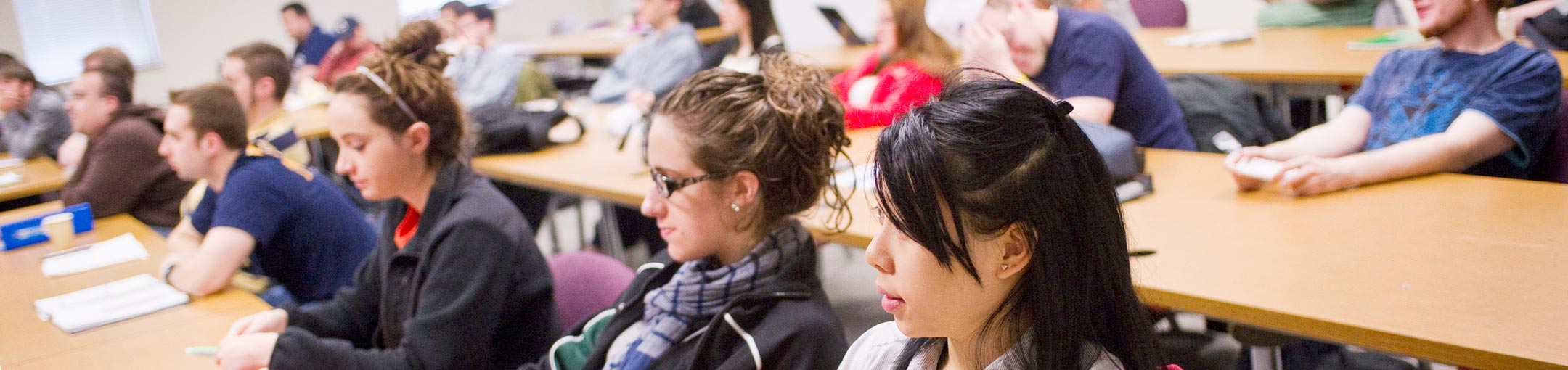 Students at long desks look toward the front of a classroom.