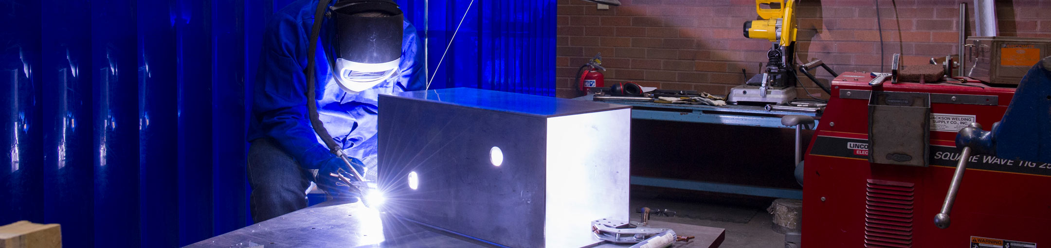 A person wearing a welding helmet welds a metal box.