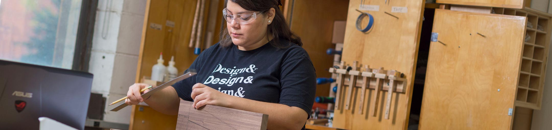 Student with ruler and pencil in hand makes measurements on a piece of wood.