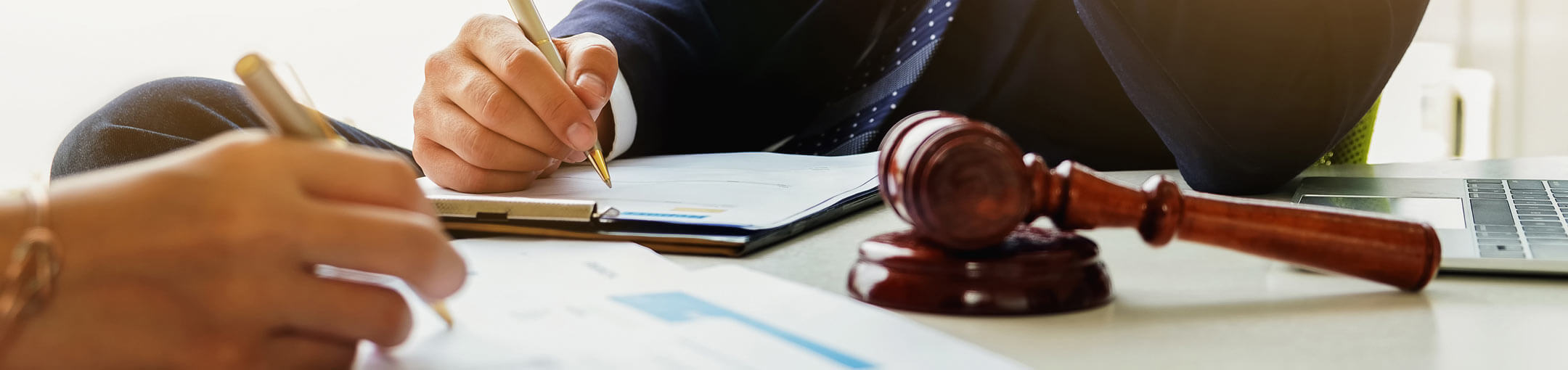 Close-up photo of two people sitting and writing at a table, which also has a gavel on it.