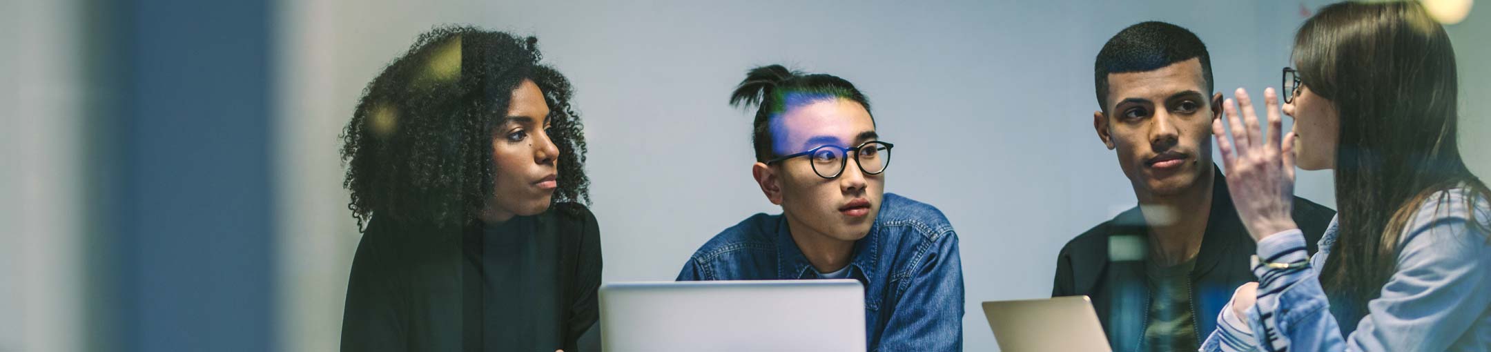 Four students talk while sitting in front of 2 laptops.