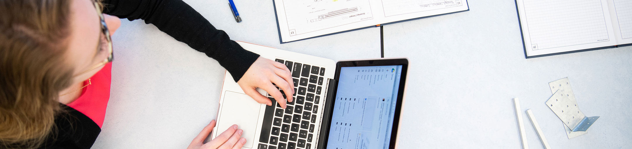 Top down view of a person sitting at a table working on their laptop.