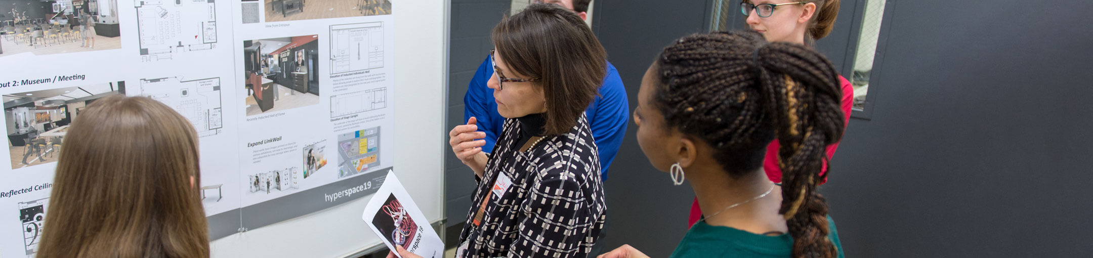 Students with their professor look at a poster presentation.