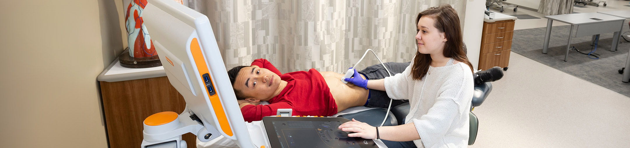 A woman using an ultrasound wand on a man who is looking at the monitor.