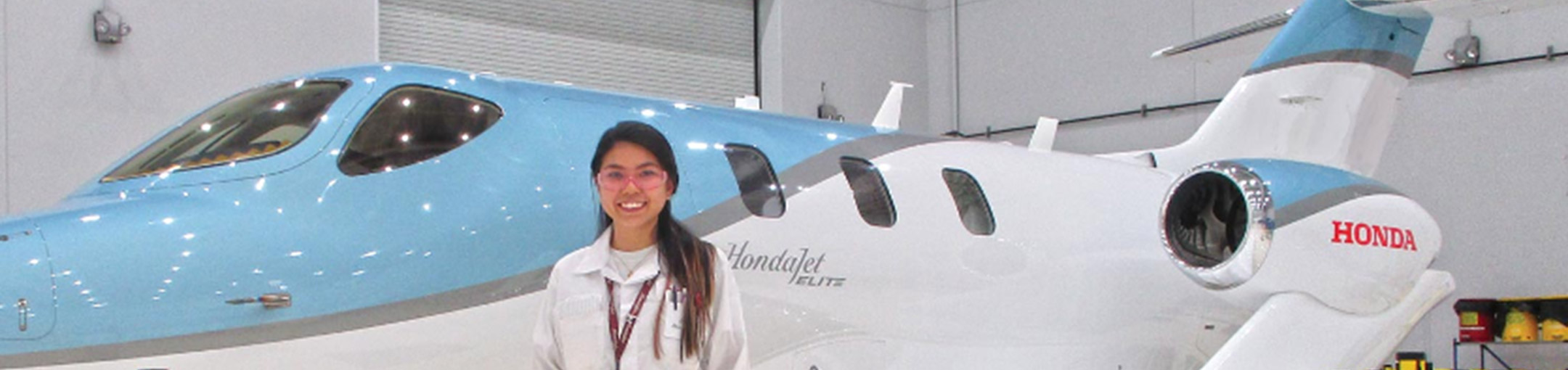A student stands in front of an airplane with the Honda logo on it.
