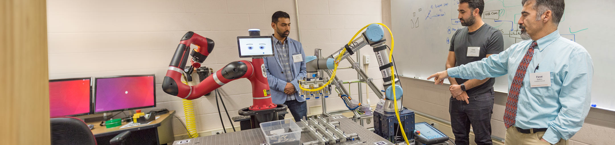 Students and professor work with robots with mechanical arms.
