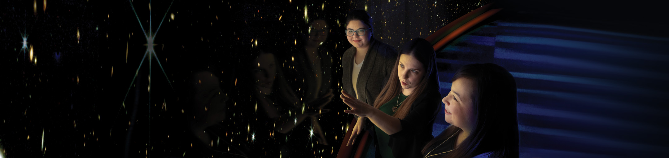 Three people look at a large projection wall of stars.