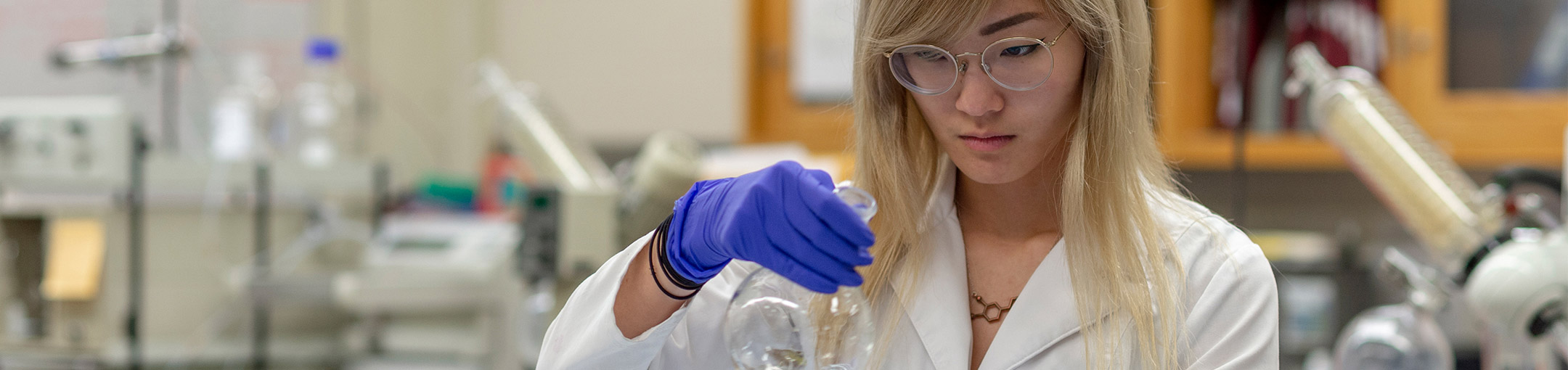 A purple-gloved students looks at the contents of a beaker.