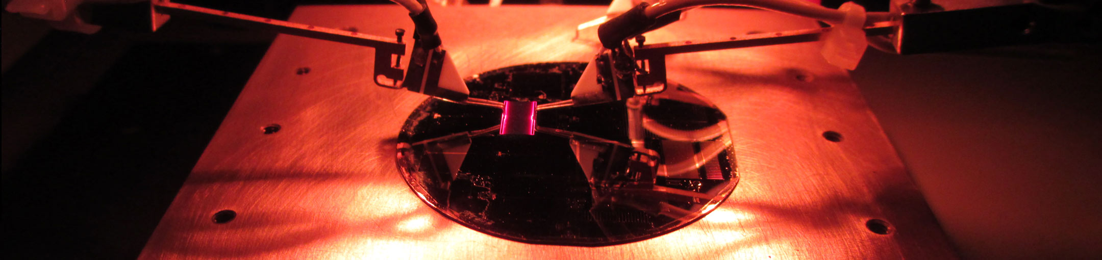 A close-up photo of clamps holding something purple and square over a reflective plate.