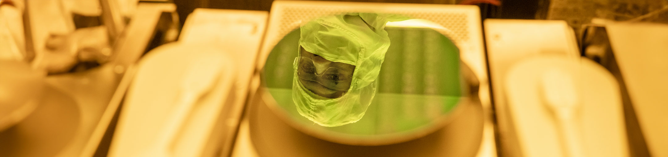 A student in a bunny suit and goggles is reflected in a wafer.
