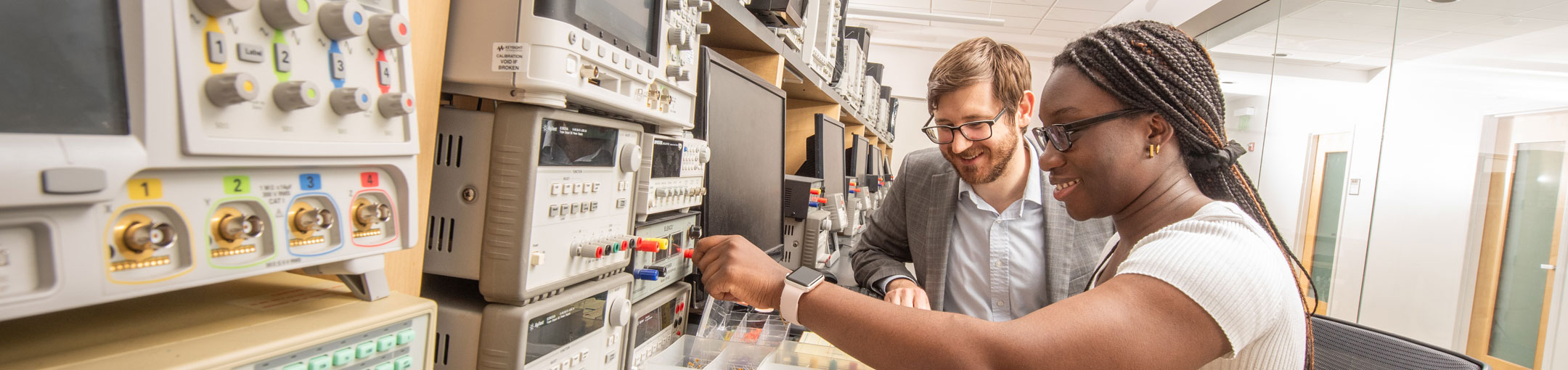 Student and professor work in front of electrical devices with various colored knobs.