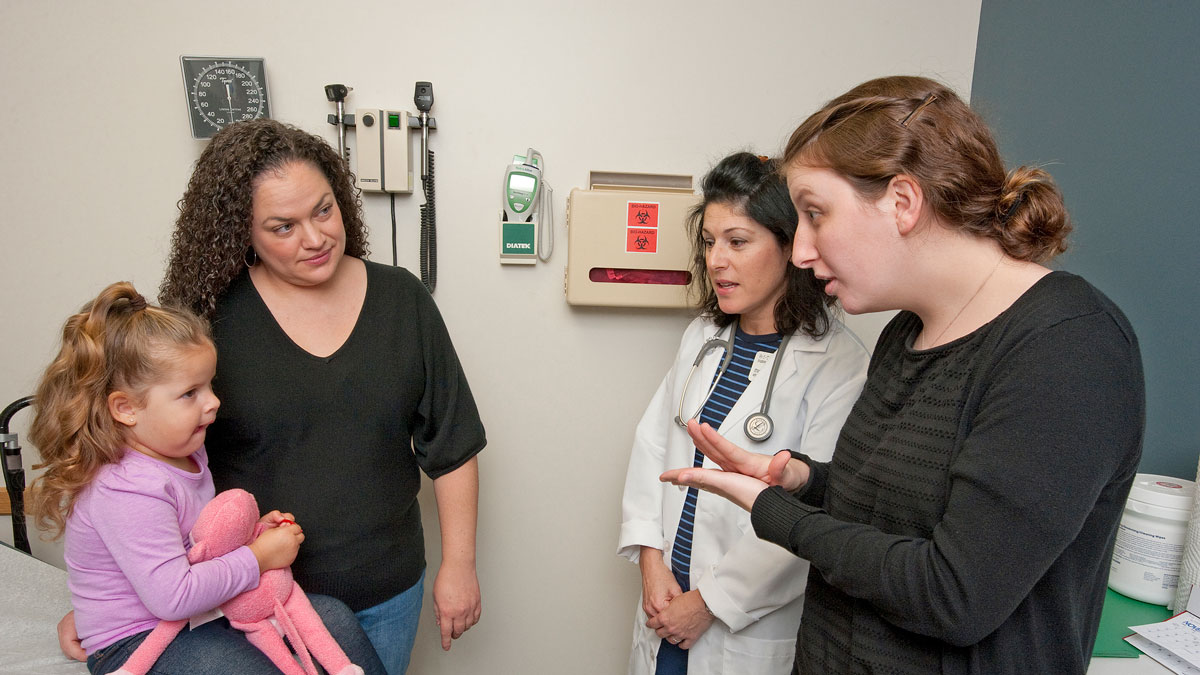 Doctor wearing lab coat and stethoscope talking to two women and young girl.