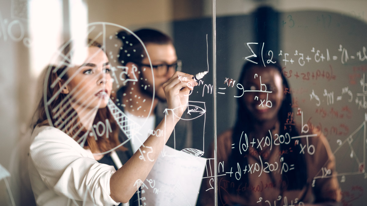 A student writes on a see-through board with mathematical formulas on it.