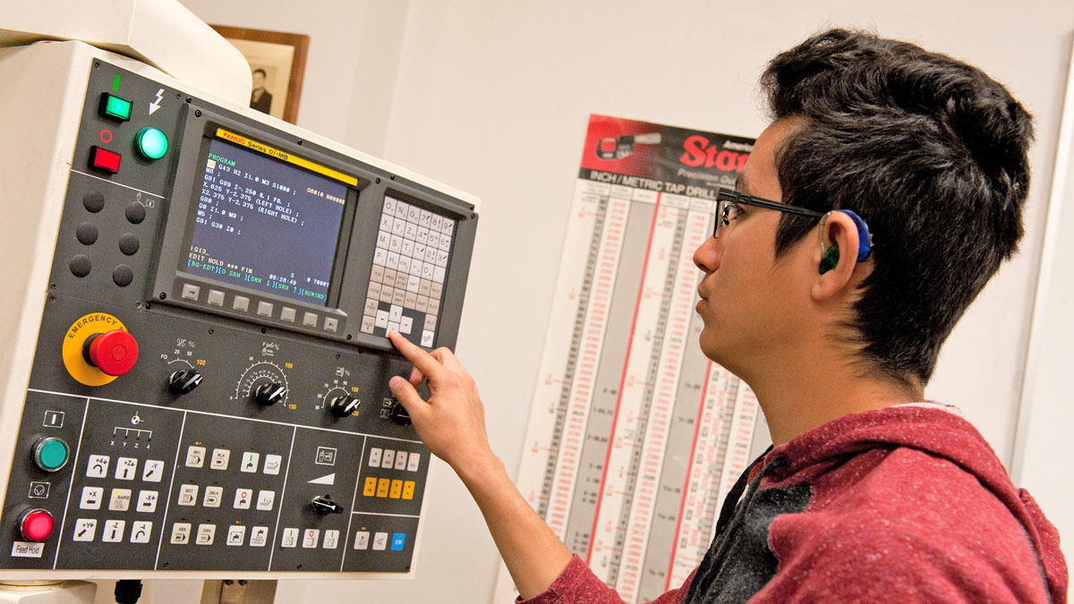 A student wearing a hearing aid uses a machining device.