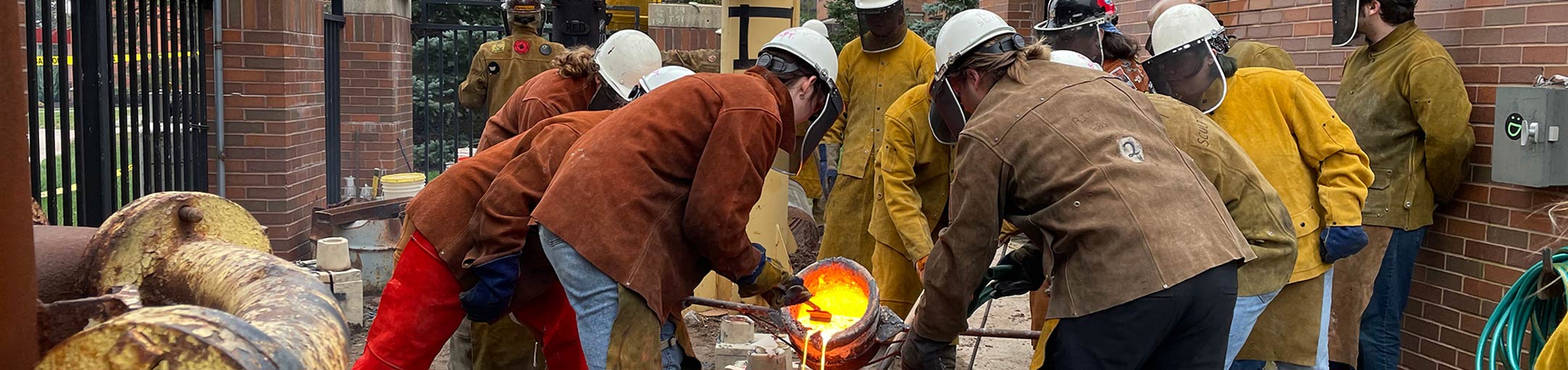 Students wearing protective gear pouring molten liquid into forms.