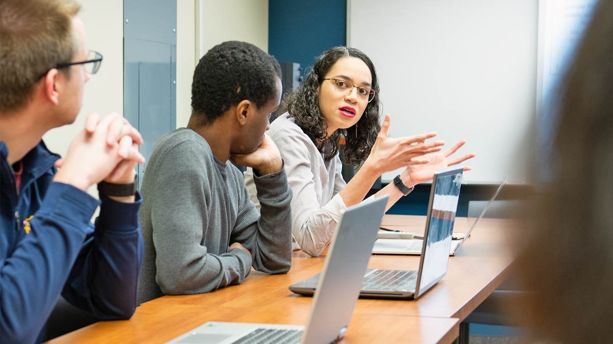 Students talk in front of their laptop computers.
