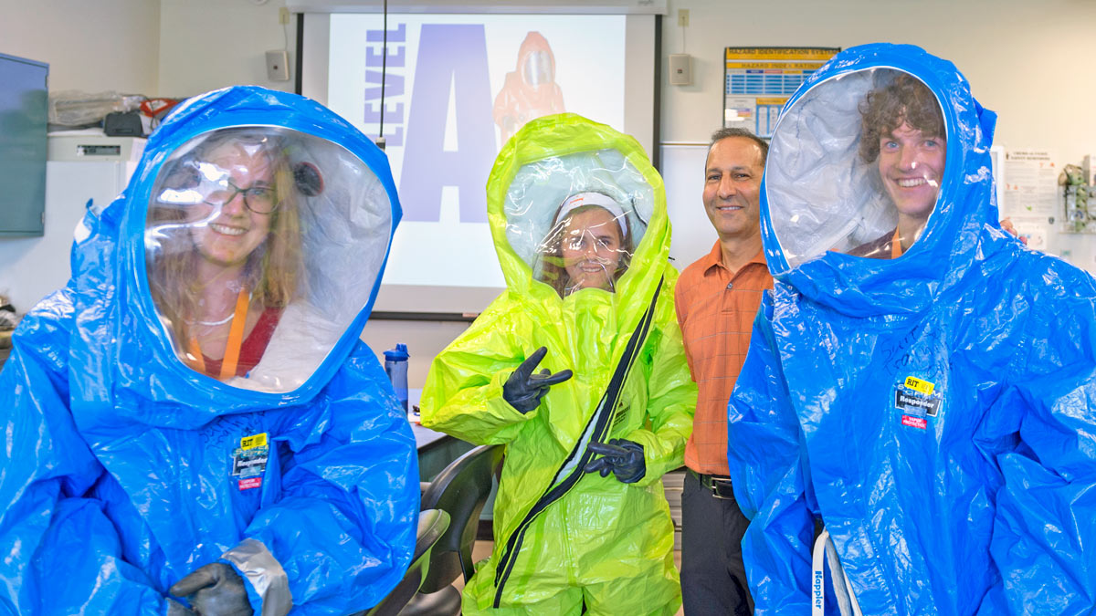 Students and teachers work in a lab, some wearing protective clothing.