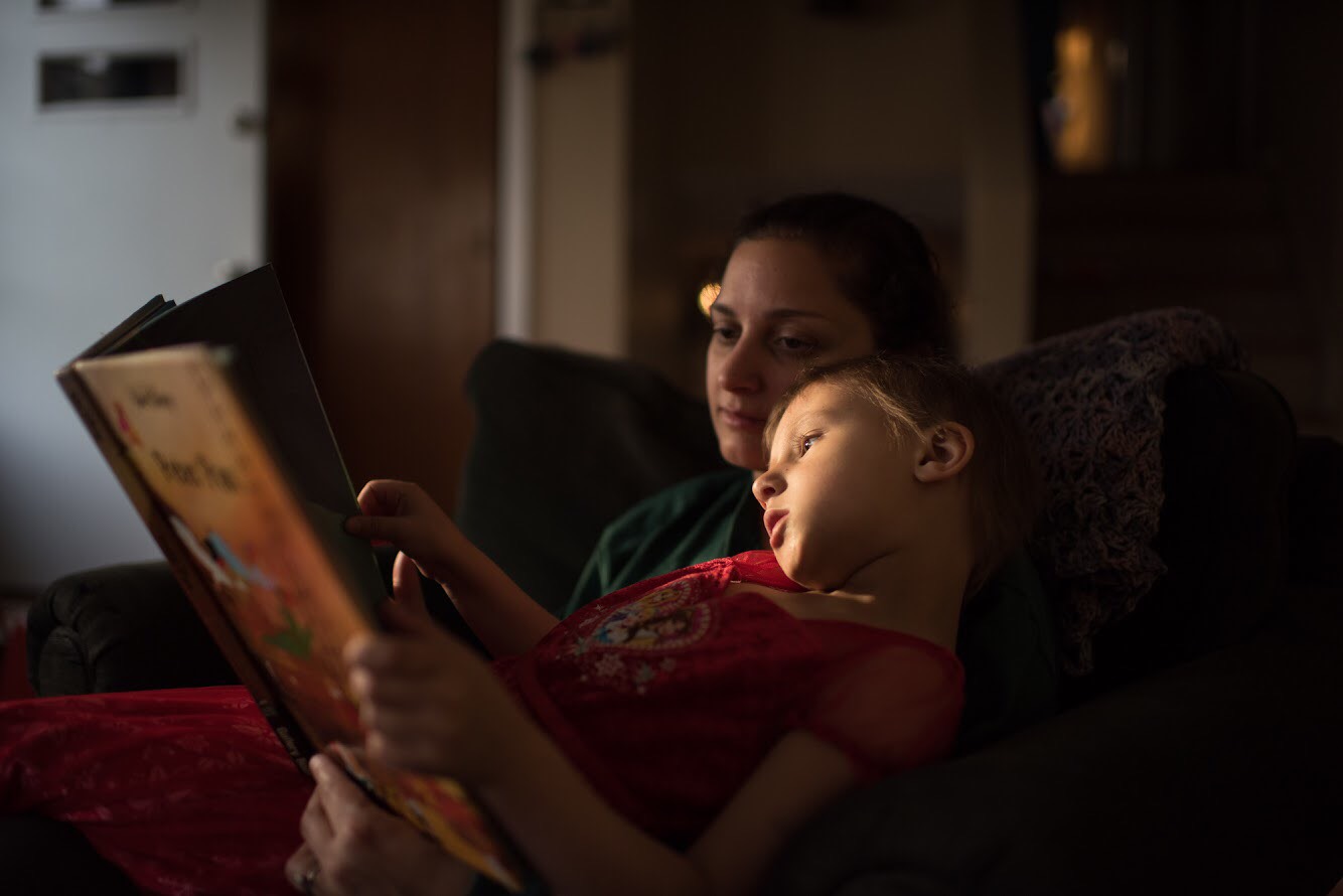 A photo of a young girl reading a book with her mother.