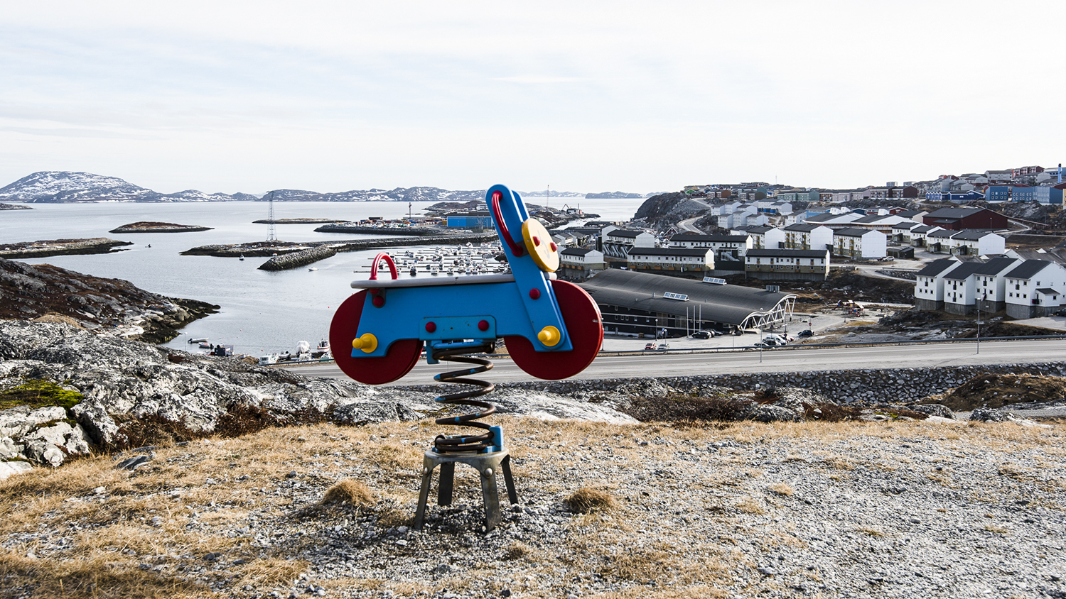 A playground toy with water, mountains and houses in the background.