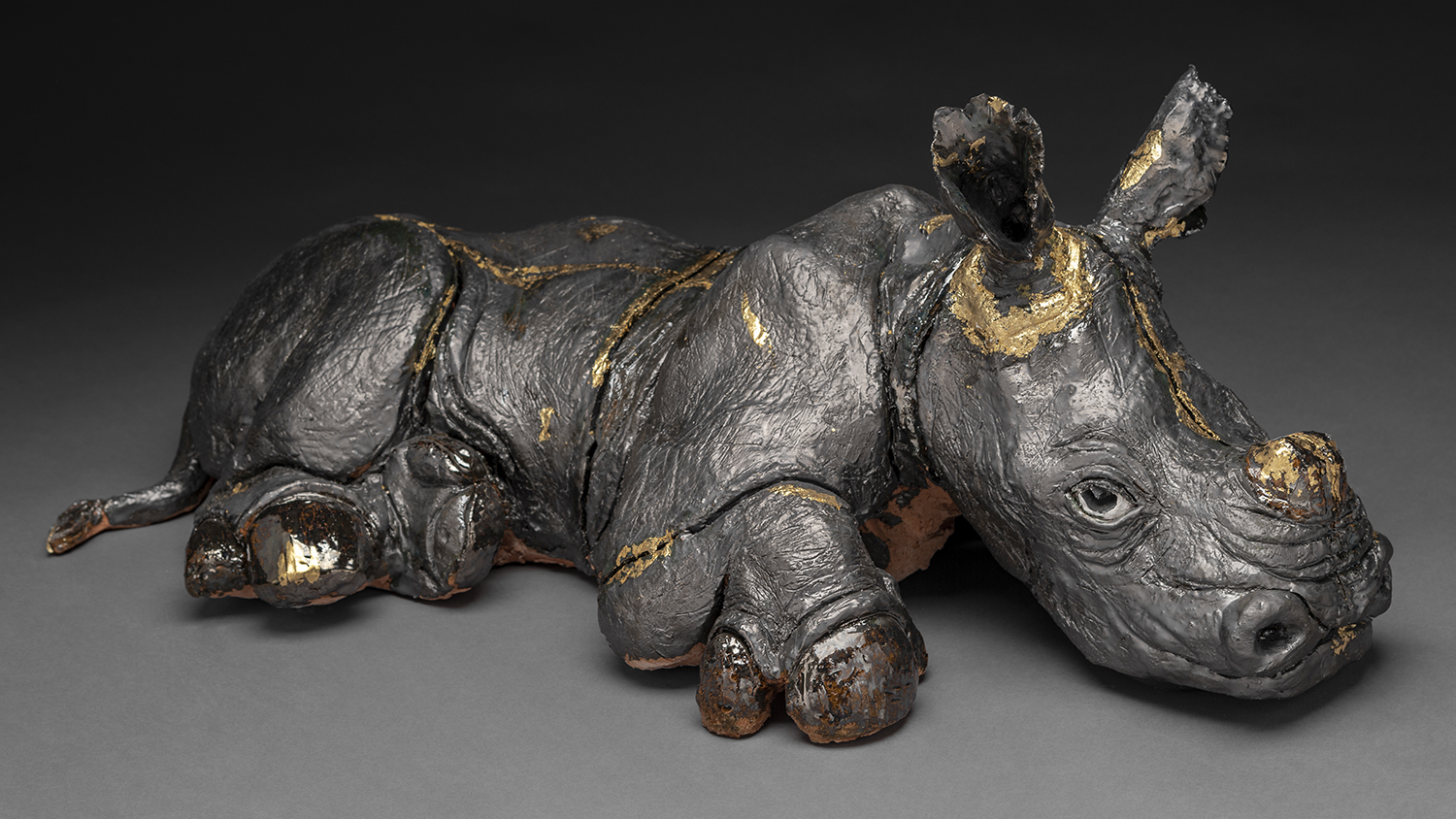 A sculpture a baby rhino laying down.