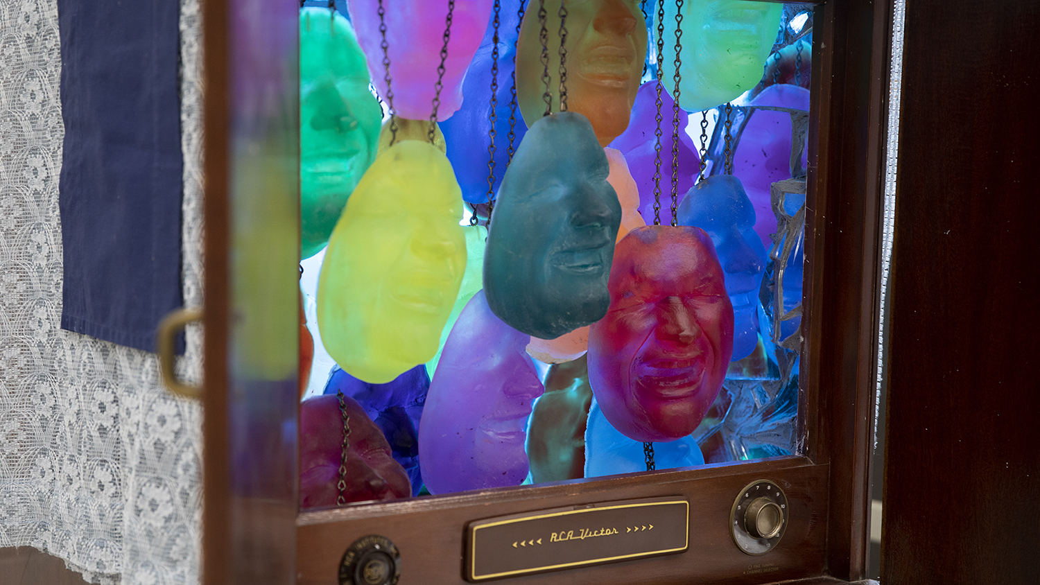 A grouping of colorful sculpted masks dangle from chains inside a retro television.