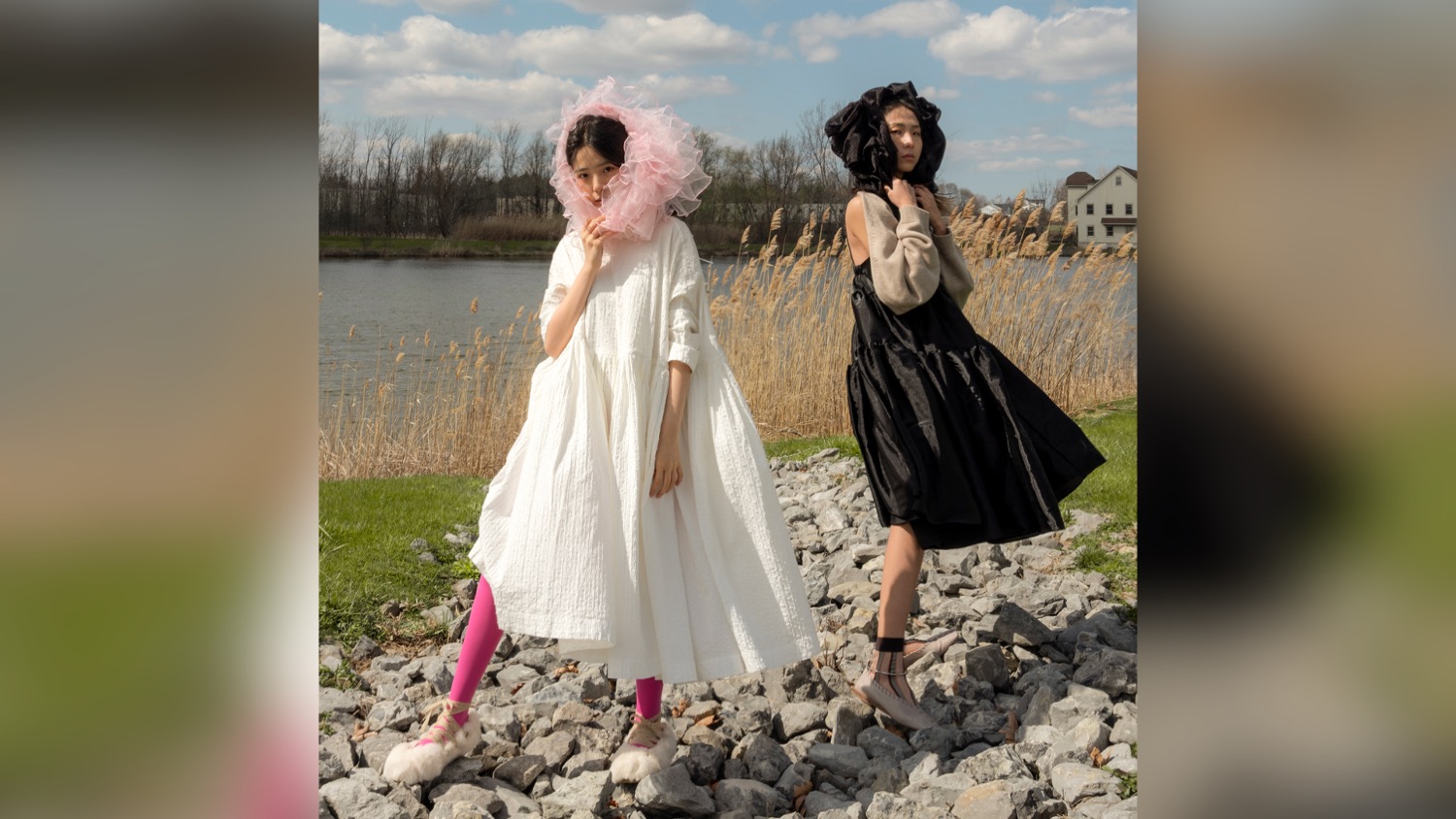 Two people dressed in dresses stand in front of a body of water.