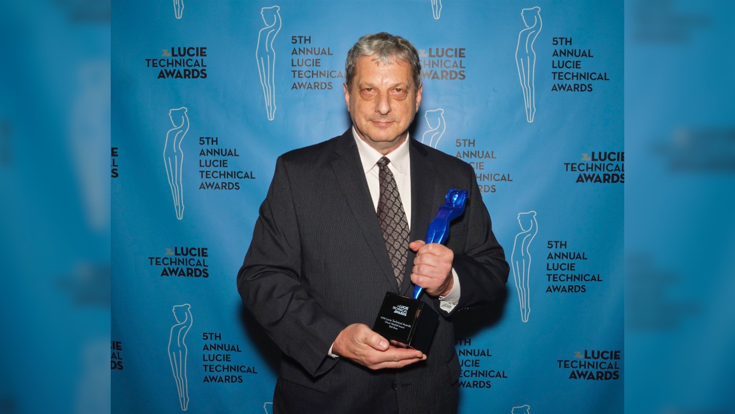 Faculty Bob Rose, dressed in a suit and tie, holds his Chuck Westfall Technical Education Award at the Lucie Awards. He won the award for advancing the photographic industry.