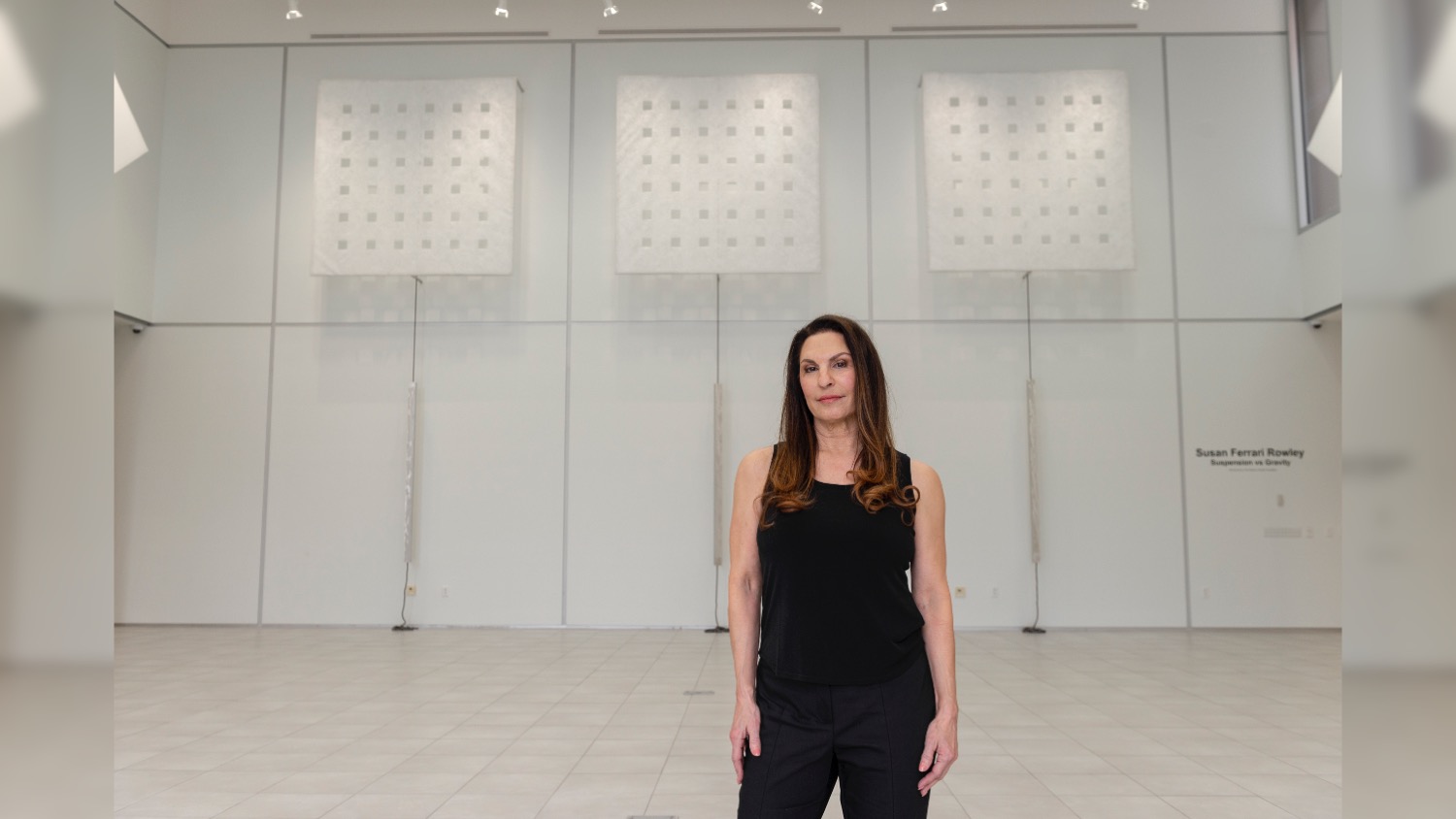 Susan Ferrari Rowley poses for a portrait, with her exhibition in University Gallery as the backdrop.